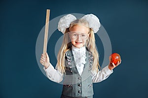 Funny little girl in school uniform wearing eyeglasses imitates a strict teacher against blue background. Looking at camera.