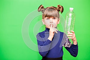 Funny little girl with shocked face and hand near head holding plastic bottles and looking confused at camera isolated over green