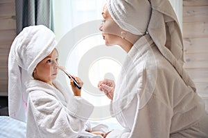 Funny little girl in soft bathrobe powdering her nose