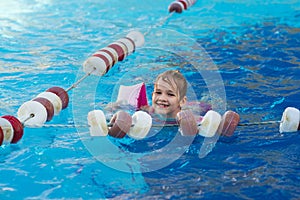 a funny little girl swims in inflatable armbands in a pool near the buoys.