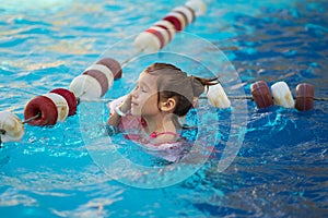 a funny little girl swims in inflatable armbands in a pool near the buoys.