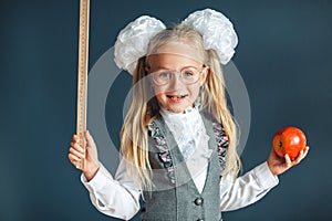 Funny little girl wearing eyeglasses imitates a strict teacher against blue background. Looking at camera. School concept. Back to