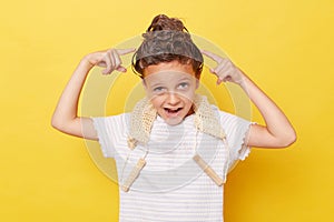 Funny little girl with wet hair wearing casual white T-shirt standing isolated over yellow background showing her hairbun with