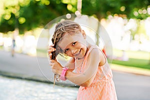 Funny little girl wetting hair in fountain hot summer day