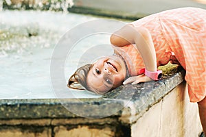 Funny little girl wetting hair in fountain hot summer day photo