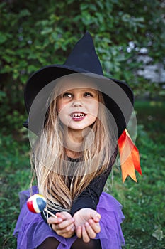 Funny little girl in witch costume eating Halloween candy outdoor