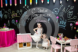 Funny little girls on a children`s holiday on the background of a blackboard with a birthday greeting Pauline photo