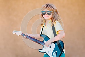 Funny little hipster musician child playing guitar. Funny rock child with guitar. Little boy in sunglasses. Kids music