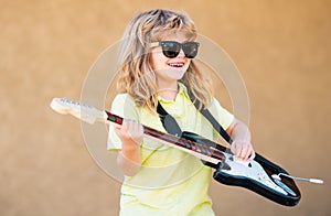 Funny little hipster musician child playing guitar. Portrait of a funny child with glasses practicing a song during a