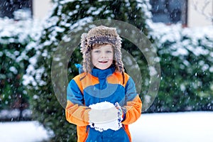 Funny little kid boy in colorful clothes playing outdoors during snowfall. Active leisure with children in winter on