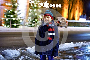 Funny little kid boy in colorful clothes playing outdoors during snowfall. Active leisure with children in winter on