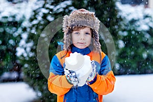 Funny little kid boy in colorful clothes playing outdoors during snowfall. Active leisure with children in winter on