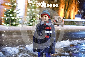 Funny little kid boy in colorful clothes playing outdoors during snowfall. Active leisure with children in winter on