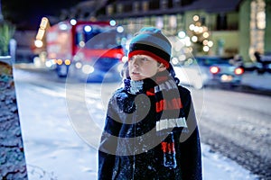 Funny little kid boy in colorful clothes playing outdoors during snowfall. Active leisure with children in winter on