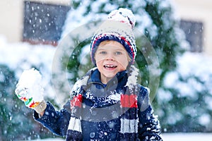 Funny little kid boy in colorful clothes playing outdoors during strong snowfall