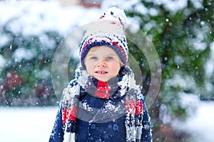 Funny little kid boy in colorful clothes playing outdoors during strong snowfall