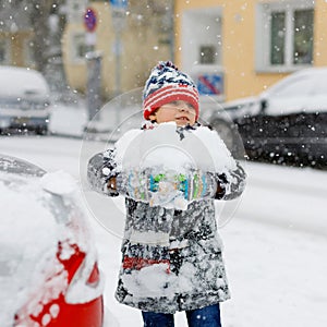 Funny little kid boy in colorful clothes playing outdoors during strong snowfall. Active leisure with children in winter