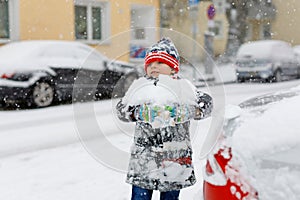 Funny little kid boy in colorful clothes playing outdoors during strong snowfall. Active leisure with children in winter
