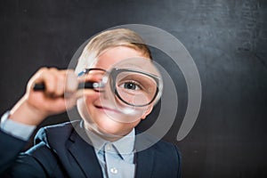 Funny little kid boy looking through a magnifying glass. Big eye. Back to school. Child curiosity