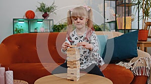 Funny little one teen kid girl play wooden tower blocks bricks game at home in modern living room