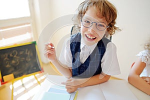 Funny little schoolboy in glasses sits at a school desk.