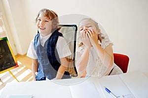 Funny little schoolchildren, boy and girl, sit at one desk.