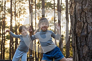 Funny little sisters peeking out from behind tree in winter park. Cute smiling child playing hide and seek in the forest. Children