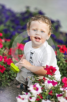 Funny little smiling boy sitting with toy shovel on flower bed on warm sunny day. Outdoors. Environment concept.