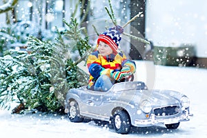 Funny little smiling kid boy driving toy car with Christmas tree.