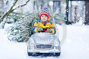 Funny little smiling kid boy driving toy car with Christmas tree.