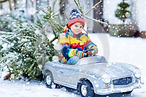 Funny little smiling kid boy driving toy car with Christmas tree.