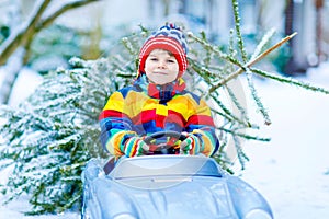 Funny little smiling kid boy driving toy car with Christmas tree. photo