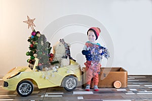 Funny little smiling kids driving toy car with Christmas tree. Happy child in colour fashion clothes bringing hewed xmas tree from