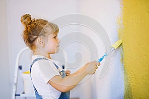 Funny little toddler girl painting the wall with color in new house. Family repair apartment home. Happy baby child