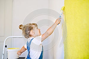 Funny little toddler girl painting the wall with color in new house. Family repair apartment home. Happy baby child