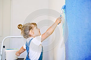 Funny little toddler girl painting the wall with color in new house. Family repair apartment home. Happy baby child