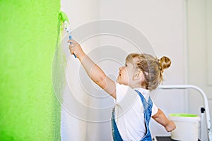 Funny little toddler girl painting the wall with color in new house. Family repair apartment home. Happy baby child