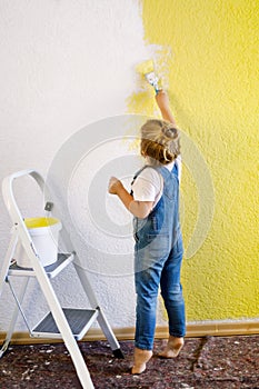 Funny little toddler girl painting the wall with color in new house. Family repair apartment home. Happy baby child