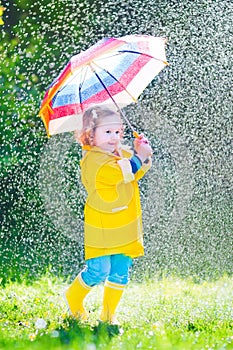 Funny little toddler with umbrella playing in the rain