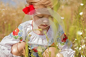 Funny little Ukrainian Caucasian girl in an embroidered shirt playing in a meadow where wild flowers