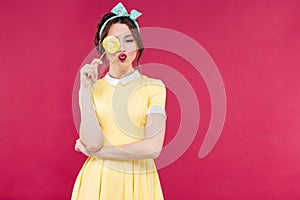 Funny lovely pinup girl covered one eye with yellow lollipop