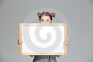 Funny lovely young woman hiding behind blank whiteboard