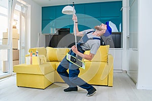 Funny male cleaning worker in special blue clothes playing with a mop as a guitar like a rockstar in the stylish cuisine