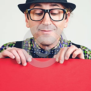 Funny male nerd looking down on empty red poster. Happy man in glasses holding sheet of paper for your text. People and