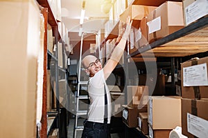 Funny male warehouse worker reaching up, putting box on a shelf