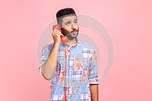 Funny man with beard wearing blue casual style shirt holding phone handset, having conversation, unbelievable news, standing with