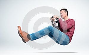 Funny man in casual clothes is driving a car with a fright grabbing the steering wheel, on light background