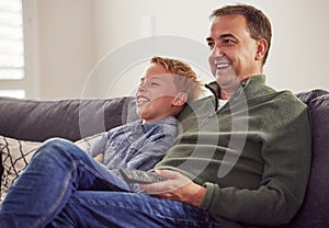 Funny, man and child together watching tv on sofa, couch and relax at home in living room. Television, movie and people