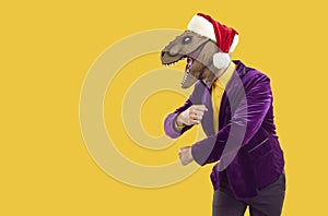 Funny man in dinosaur mask, Christmas hat and party suit dancing on copy space background