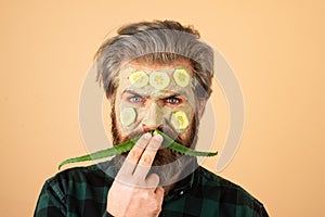 Funny man with facial mask with Cucumber and aloe vera having fun. Spa man applying facial clay mask. Funny bearded man